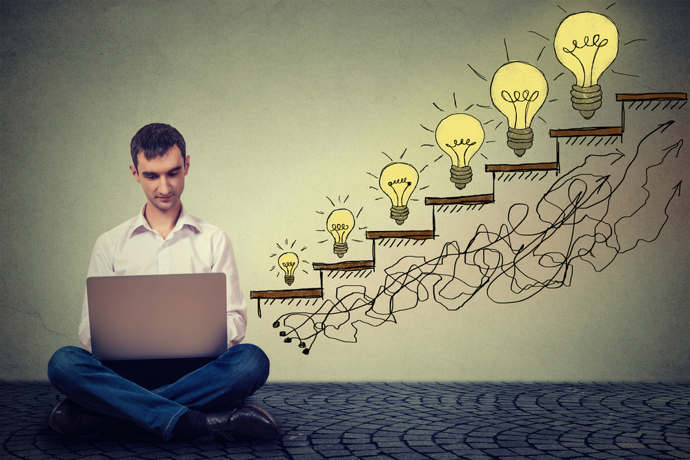 Happy young man entrepreneur working on computer sitting on a floor in his office successful in increasing internet website traffic. Promotion, company growth concept. Isolated on gray wall background Happy young man entrepreneur working on computer sitting on a floor in his office successful in increasing internet website traffic. Promotion, company growth concept. Isolated on gray wall background